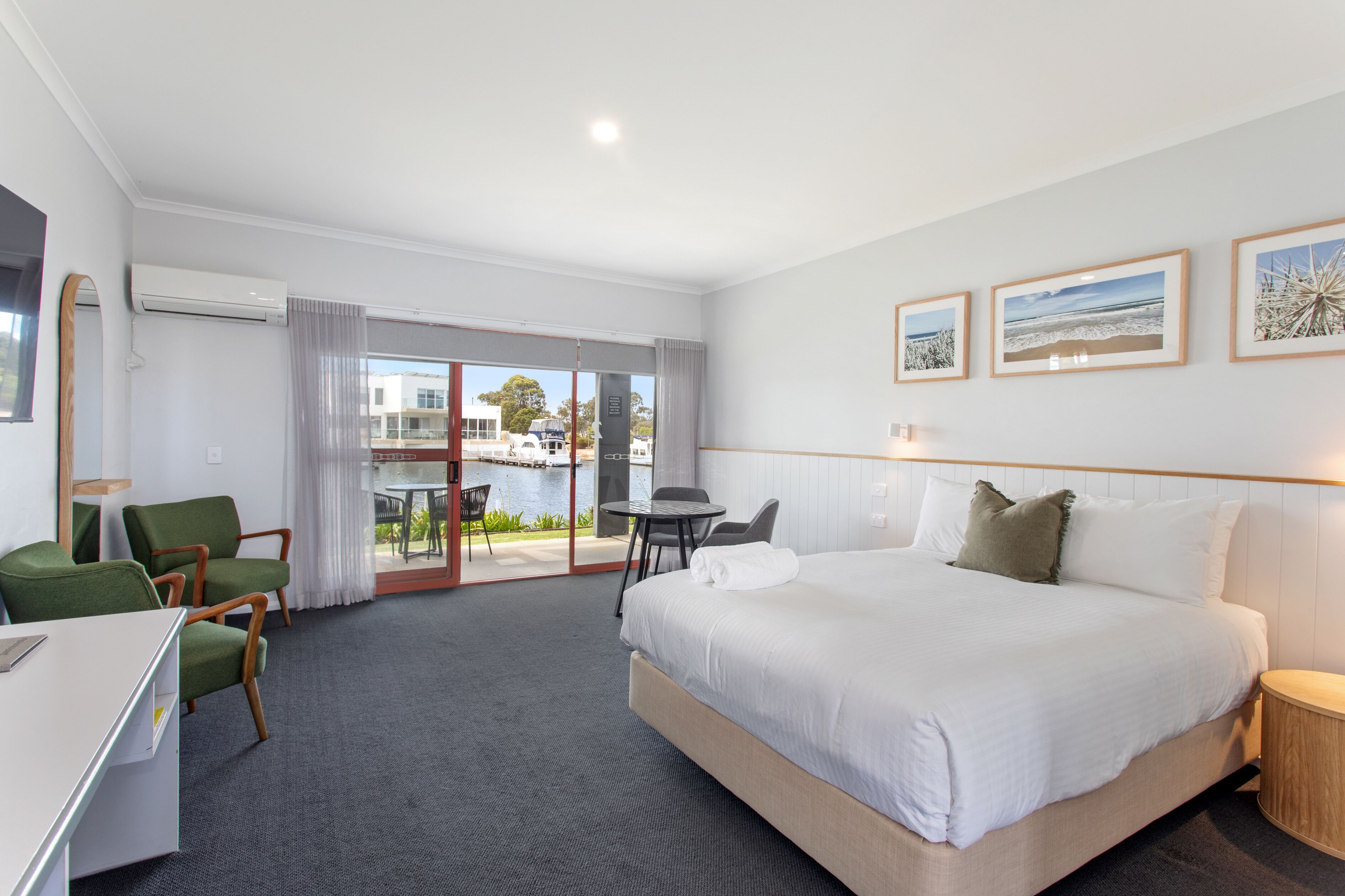 A hotel room with a large bed, a desk, green chairs, a small table, and a view of the outdoors.