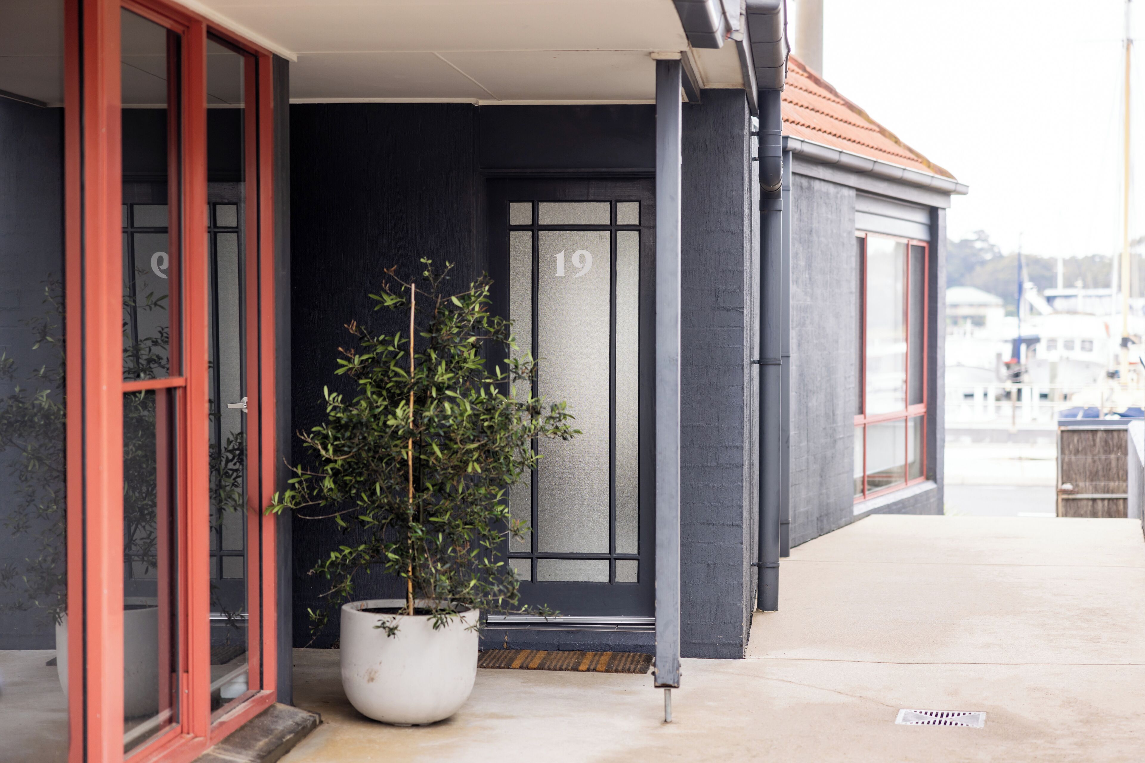 A building with a dark facade, a red-framed entrance door, and a potted plant outside.