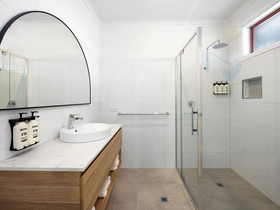 Uma casa de banho moderna com uma toucador branco, um espelho grande e zona de duche com parede de vidro.