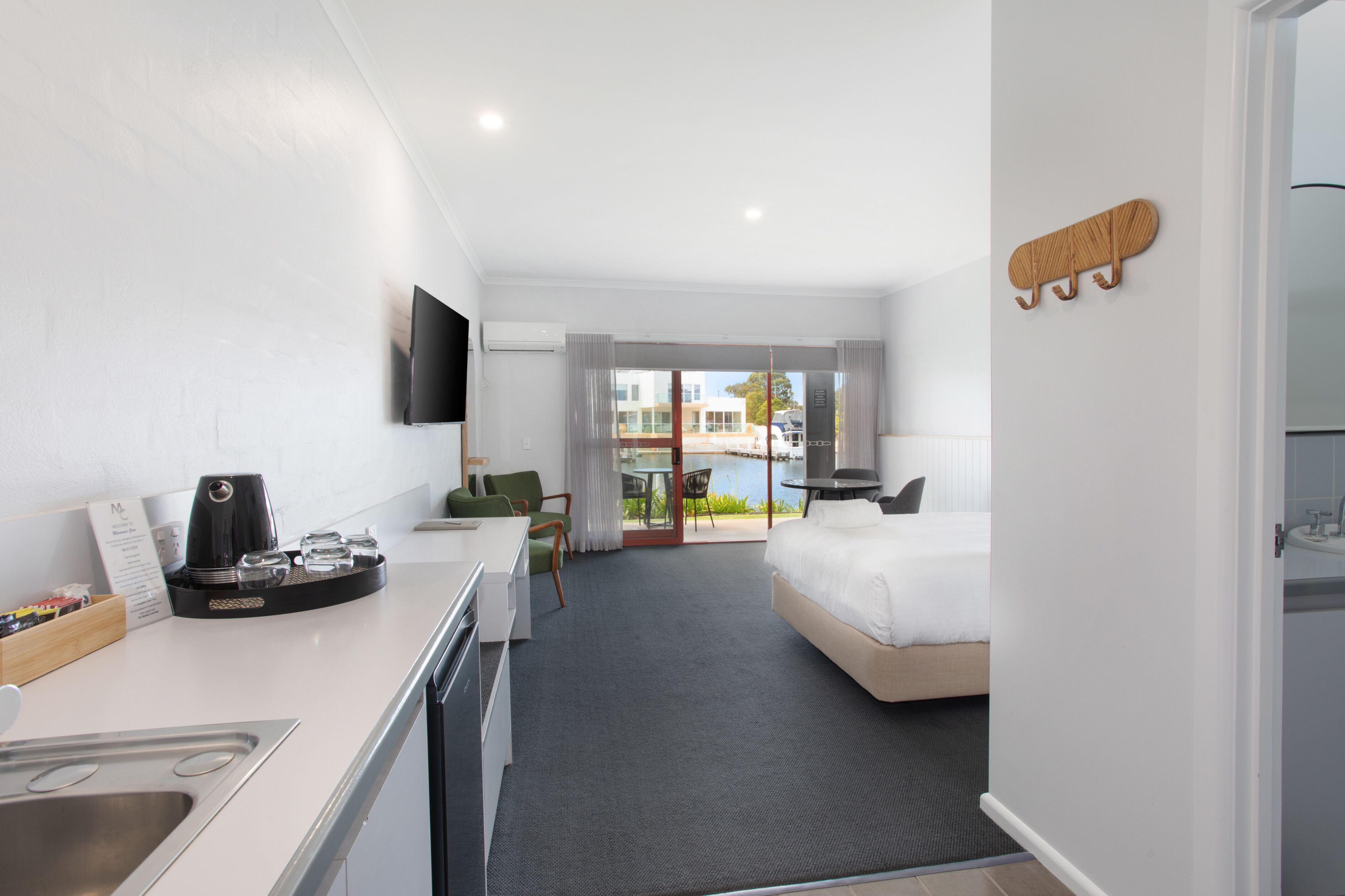 A hotel room with a kitchenette, a bed, a TV mounted on the wall, and a view through the glass door.