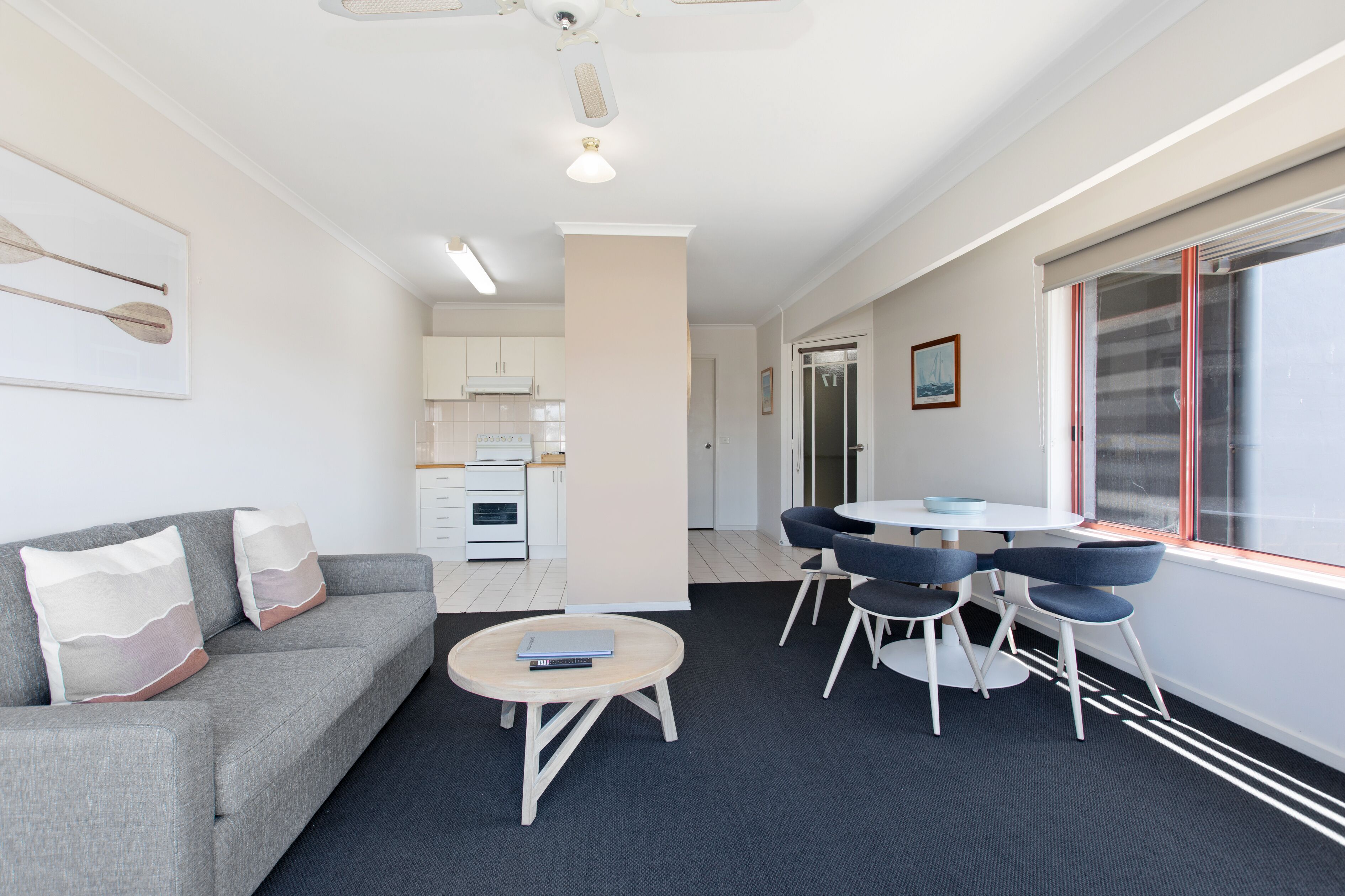 A modern living room with a grey sofa, a round coffee table, and a dining area with a white table and blue chairs.