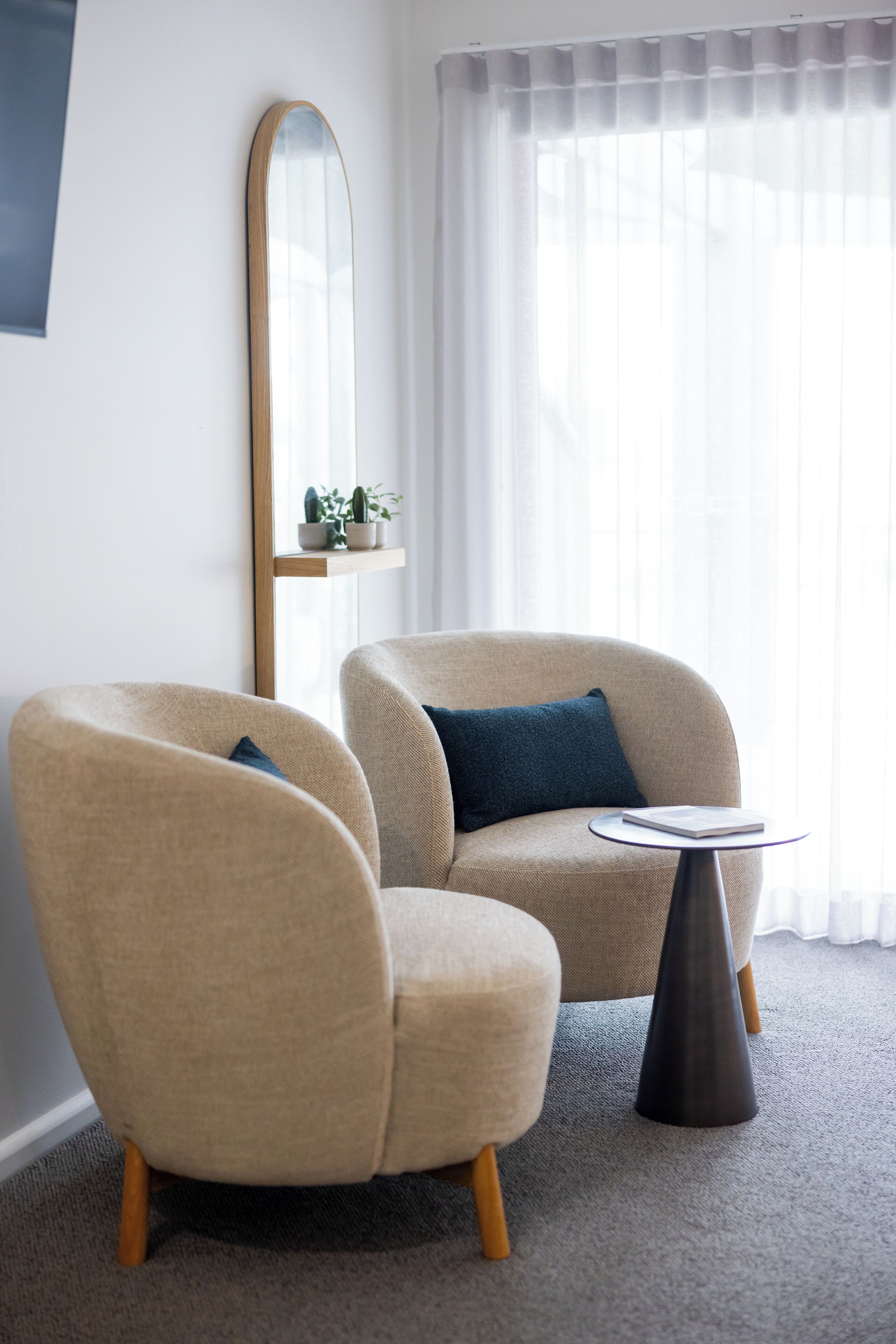 En moderne stue med to beige lænestole, et rundt sofabord og et stort spejl på væggen.