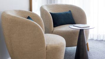 A modern living room with two beige armchairs, a round coffee table, and a large mirror on the wall.