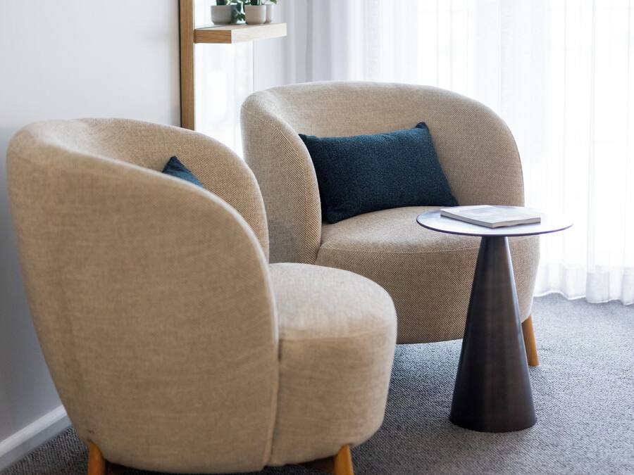A modern living room with two beige armchairs, a round coffee table, and a large mirror on the wall.