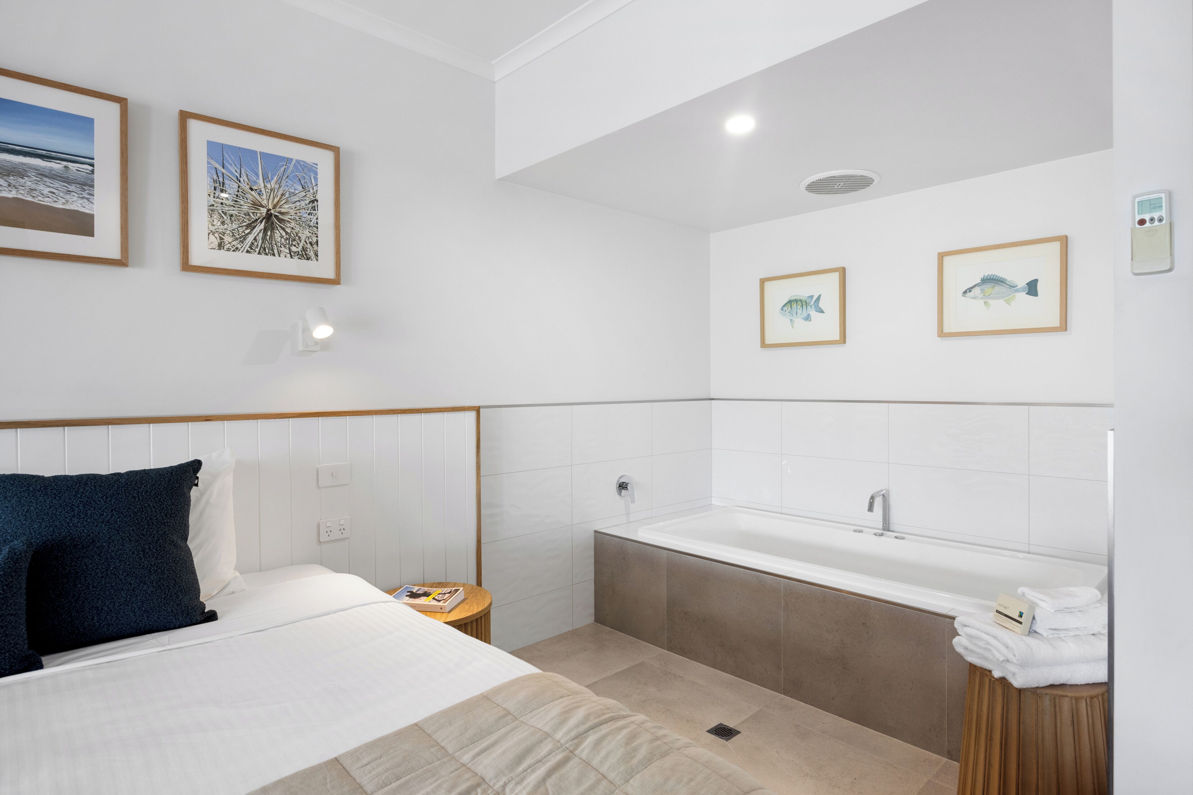 Una camera d'albergo moderna con un letto, un comodino, un tavolo di fianco al letto, un bagno con vasca e quadri appesi alle pareti.