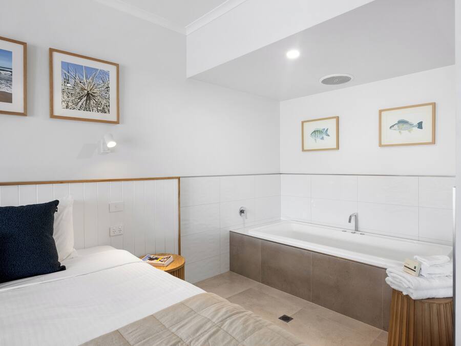 Ein modernes Hotelzimmer mit Bett, Nachttisch, Bad mit Badewanne und gerahmten Bildern an den Wänden.