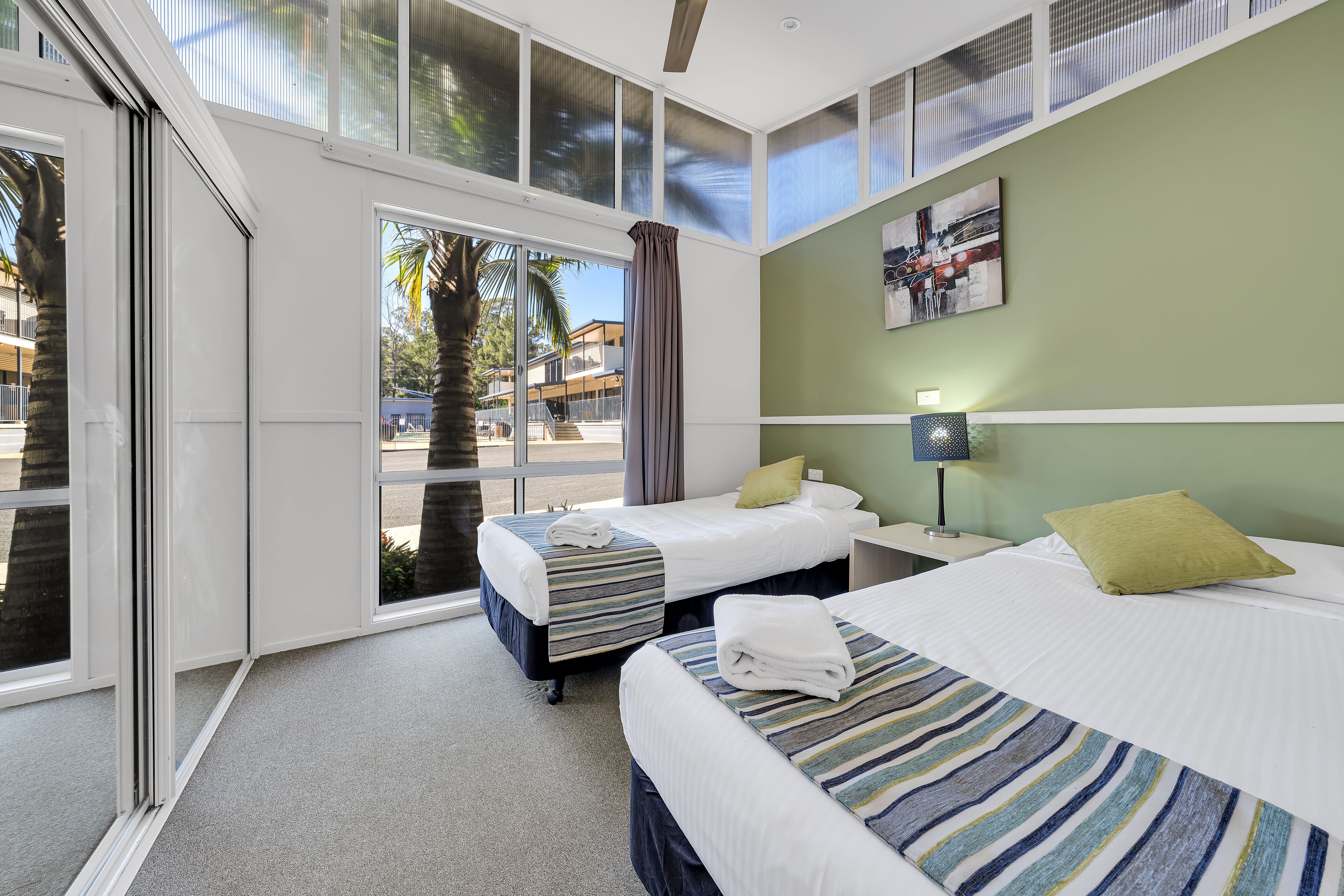 A hotel room with two beds, a large window, a view of the outside, and a painting on the wall.
