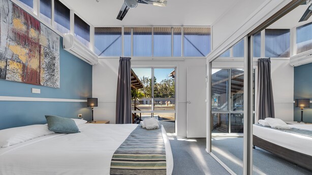 A modern hotel room with a large bed, a view through glass doors, and a ceiling fan. - Ingenia Holidays Avina (Vineyard)