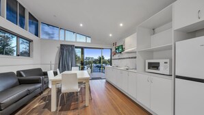 A modern kitchen with white cabinets, a dining area with a white table and chairs, and a black leather sofa. - Ingenia Holidays Avina (Vineyard)