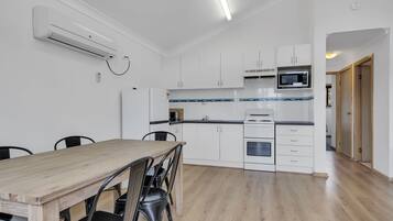 Une cuisine moderne avec des meubles blancs, un four à micro-ondes et un four encastré. On y trouve une table à manger avec des chaises et un climatiseur fixé au plafond.