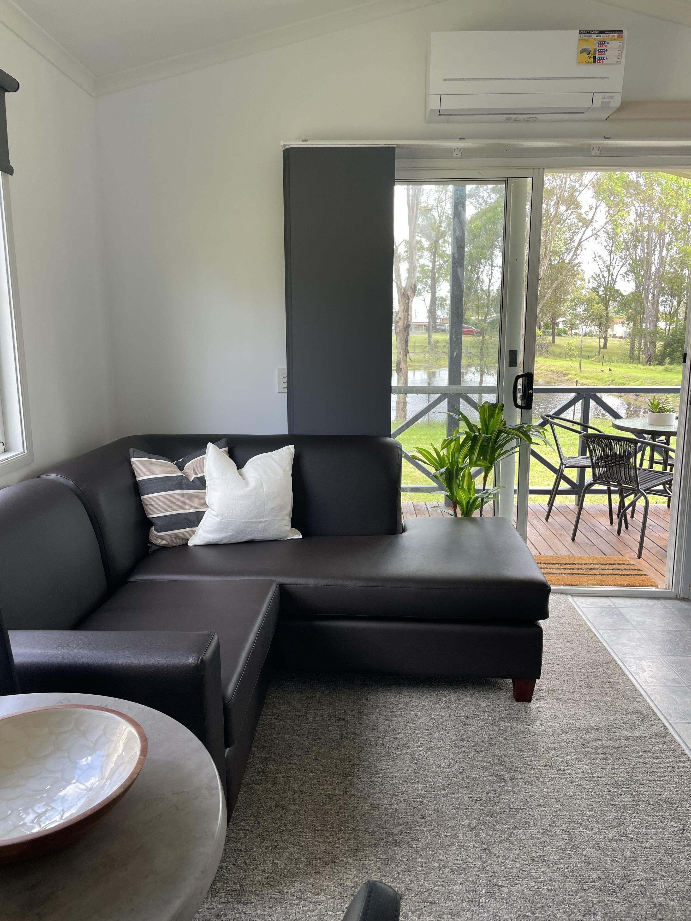 Una sala moderna con un sofá seccional, una mesa redonda de centro y vistas a una terraza con mobiliario exterior.