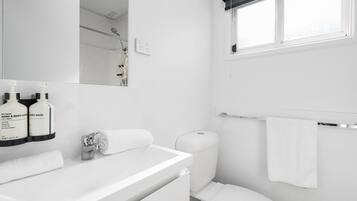 A modern bathroom with a white sink, a toilet, a towel rack, and a window with a blind.