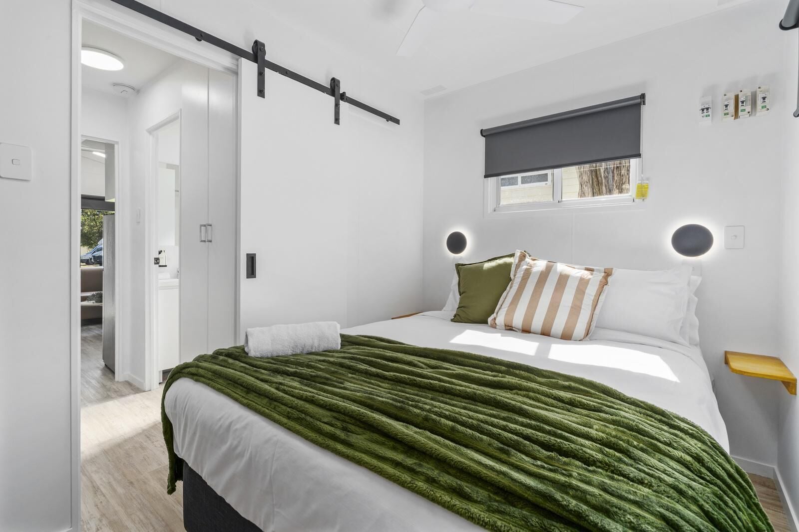 Moderni makuuhuone, jossa on sänky, vihreä heittopeitto ja ikkuna, jossa on tumma sälekaihdin.