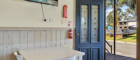 A room with a wooden panel wall, a white table with chairs, a fire extinguisher, and a door leading outside.
