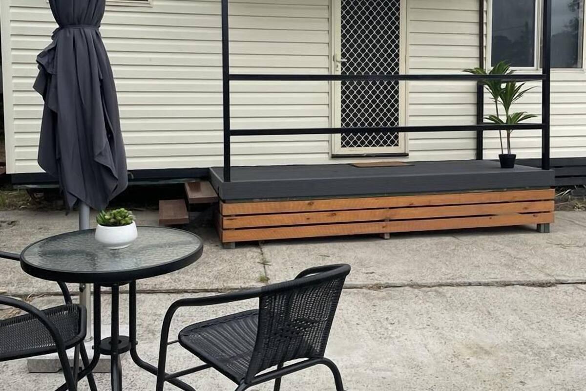 Una petita zona exterior amb seients, amb dues cadires, una taula, un porxo cobert amb una banca i una planta en test.