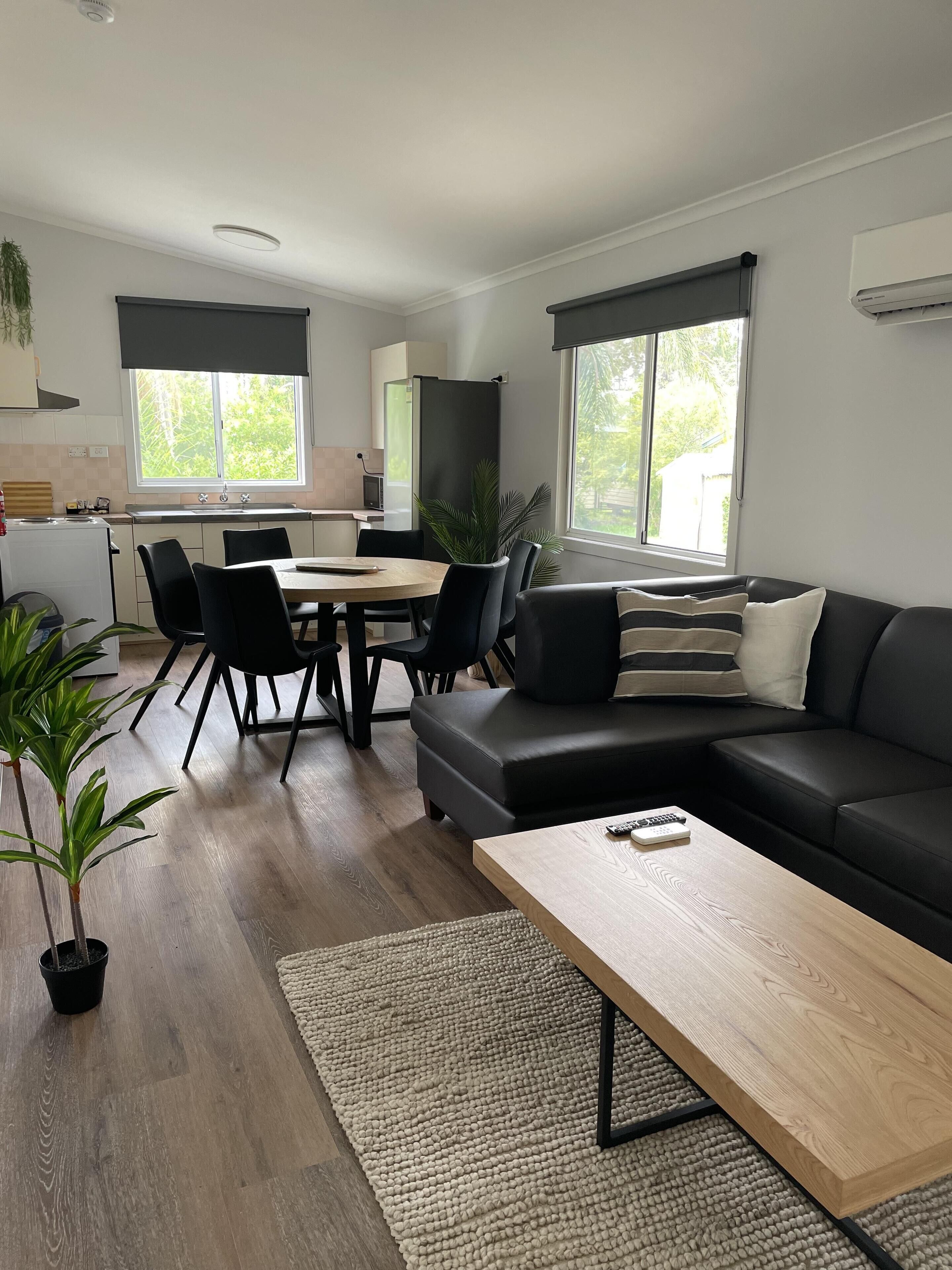A modern living room with a black sofa, a wooden coffee table, and a dining area with a table and chairs.