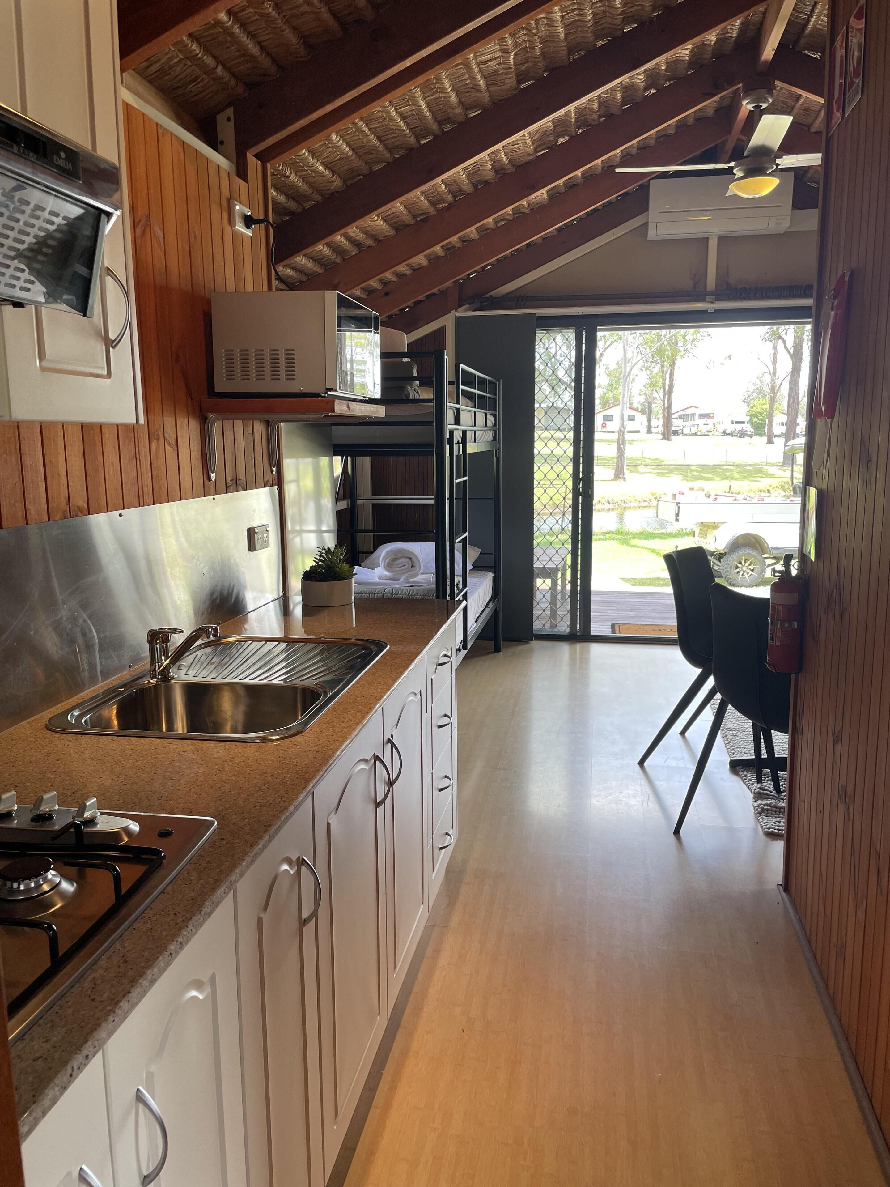 A compact kitchen with a sink, stove, and cabinets. A dining area with a table and chairs is visible through an open door.