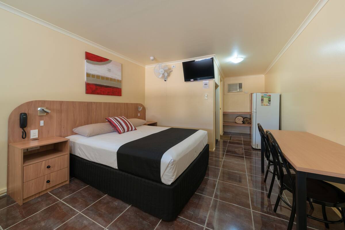Un dormitorio con cama, mesita de noche y televisor montado en la pared.