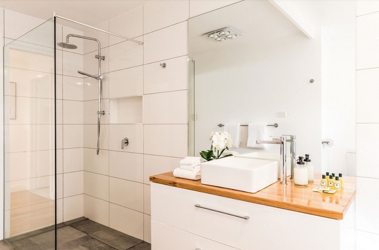 Un baño moderno con ducha de vidrio, tocador de madera con lavabo blanco y un espejo grande.