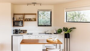 A modern kitchen with a wooden island, white cabinetry, a built-in microwave, and a window with a view of trees. - Curringa Farm (Hamilton)