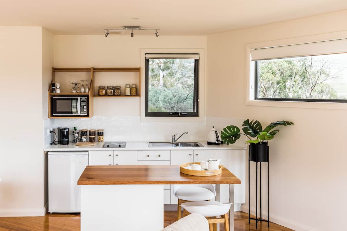 A modern kitchen with a wooden island, white cabinetry, a built-in microwave, and a window with a view of trees.