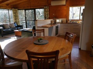 A cozy cabin interior with a wooden dining table, chairs, a sofa, and a kitchen area with a microwave and cabinets.