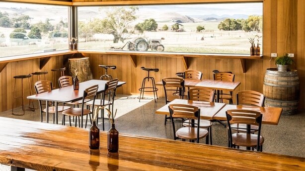 A restaurant with wooden interiors, large windows offering a view of a tractor and fields, and a rustic barrel as a decorative element. - Curringa Farm (Hamilton)