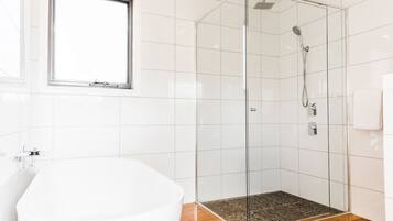 A modern bathroom with a glass-enclosed shower, a white bathtub, and a window.