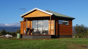A wooden cabin with a large window, a balcony, and a green door.