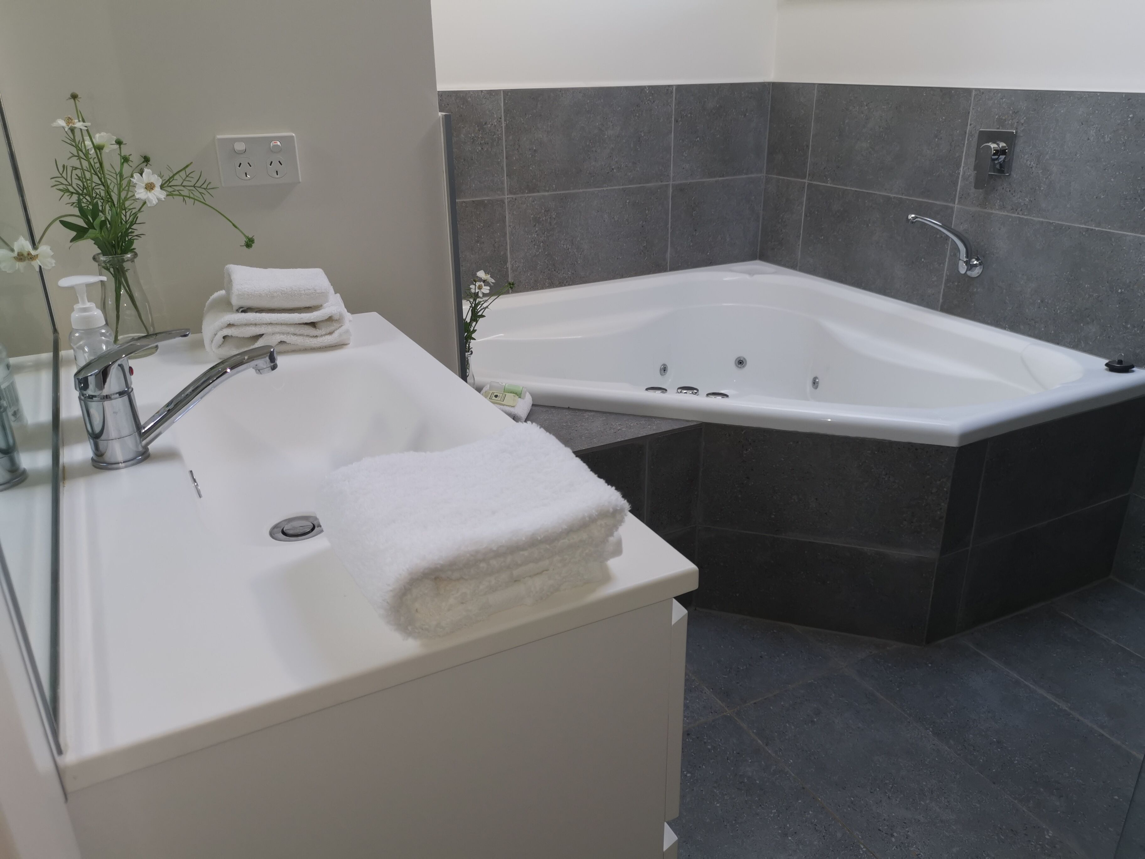 A modern bathroom with a white sink, a bathtub, and dark tiled walls.
