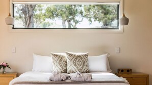 A neatly made bed with two patterned pillows, a bedside table with a vase of flowers, and a window with a view of trees. - Curringa Farm (Hamilton)