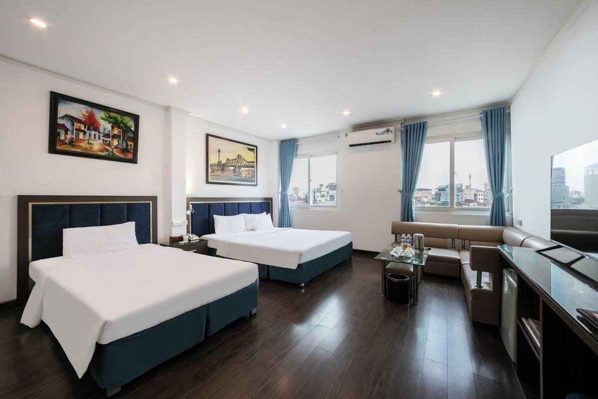 Habitación de hotel con dos camas, un sofá, una mesita y vistas a la ciudad.