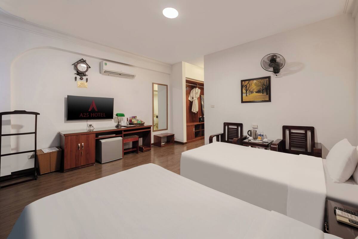 Habitación de hotel con dos camas, un escritorio, un televisor, un armario y un espejo.
