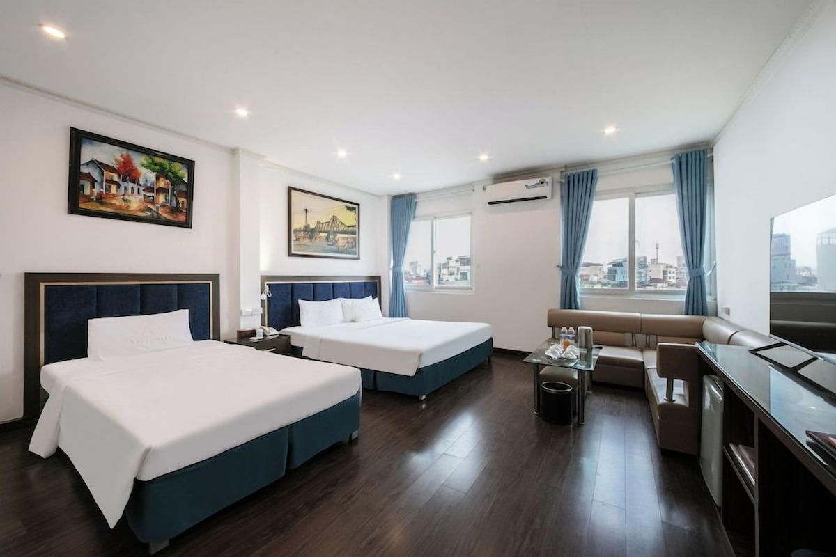 Habitación de hotel con dos camas, un sofá, una mesita y vista a la ciudad.