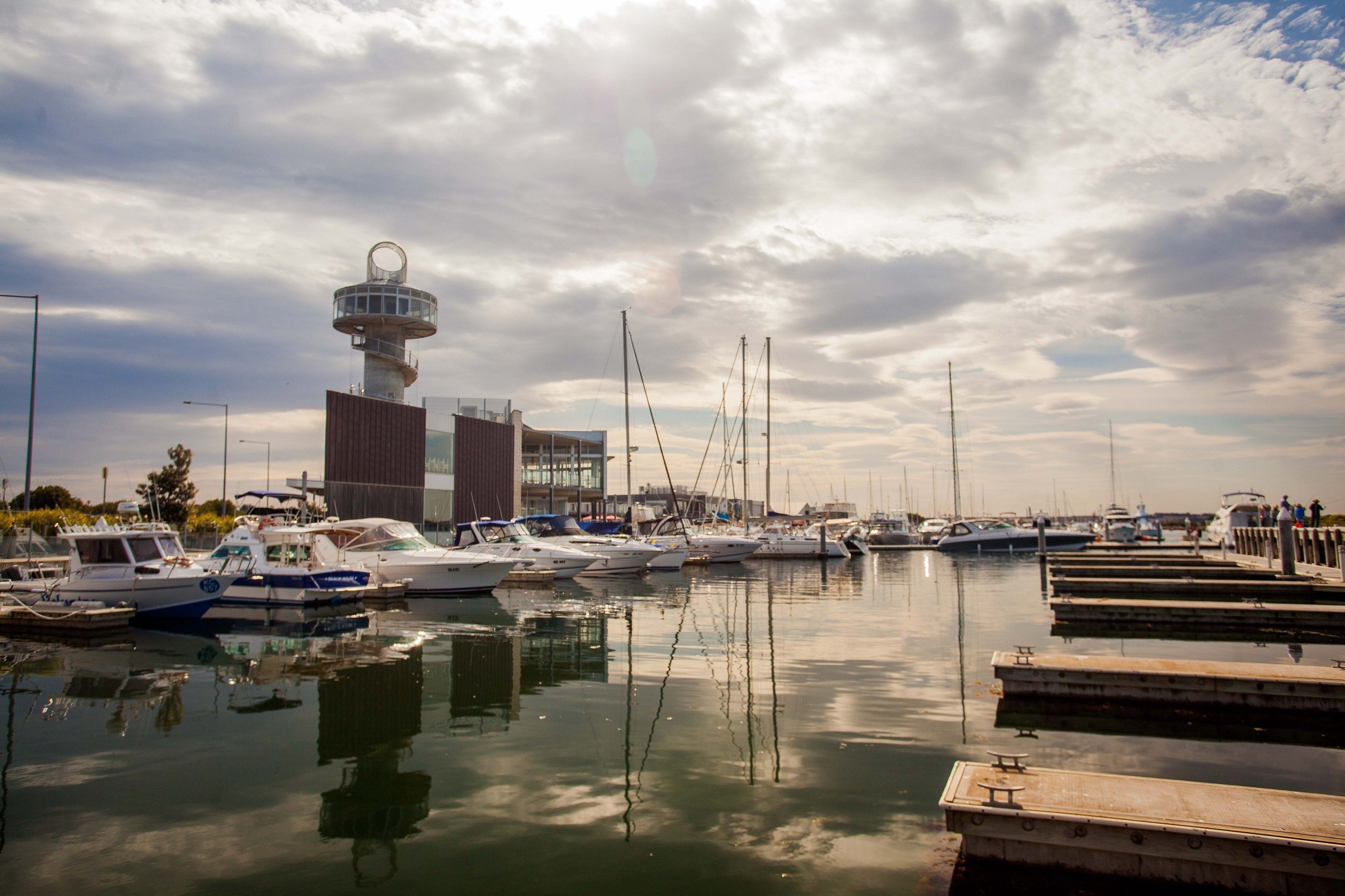 Un puerto deportivo con barcos amarrados, una torre de control y un edificio moderno con fachada de vidrio.