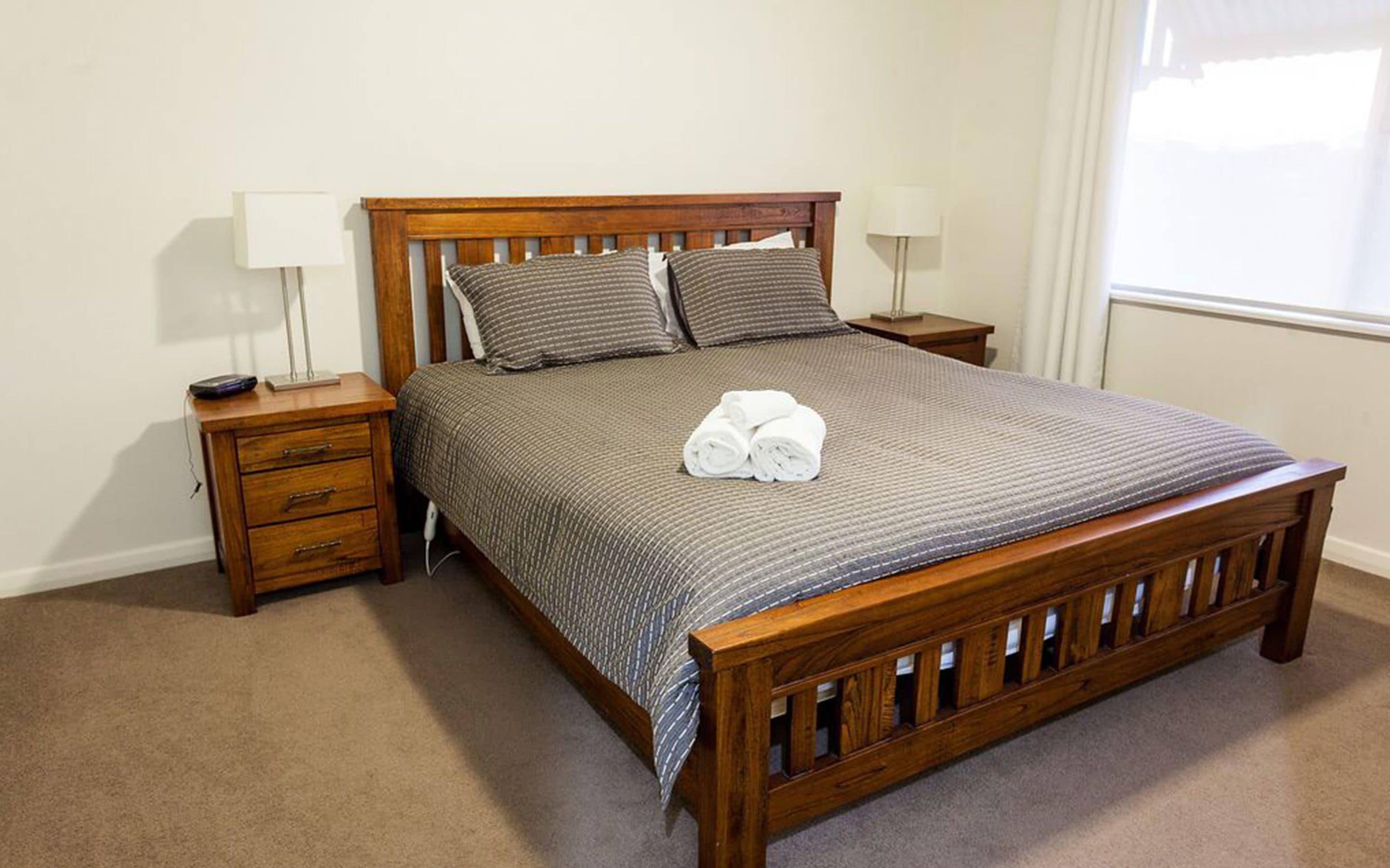 A neatly made bed with a wooden frame, two bedside tables, and a lamp on each side.