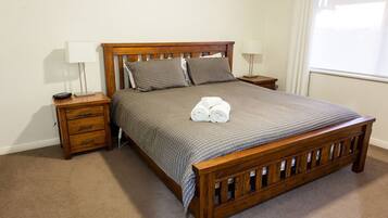 A neatly made bed with a wooden frame, two bedside tables, and a lamp on each side.