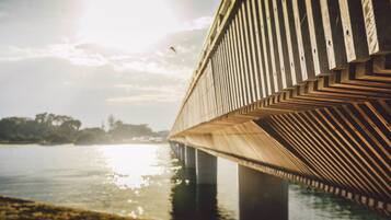 A wooden bridge with a chevron pattern, over a body of water, with a clear sky and sunlight reflecting on the surface.