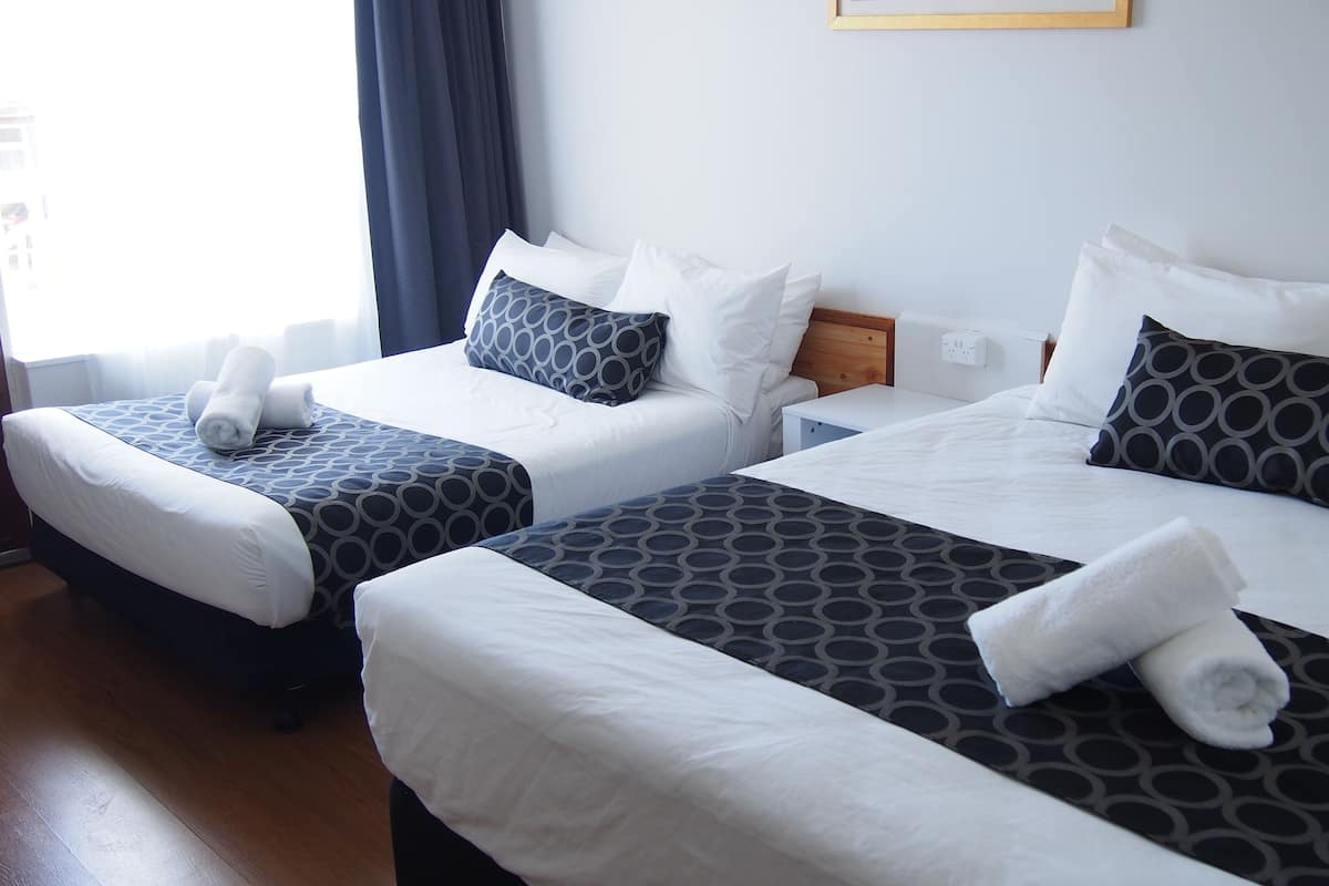 Habitación de hotel con dos camas, cada una con una colcha estampada, almohadas blancas y toallas enrolladas.