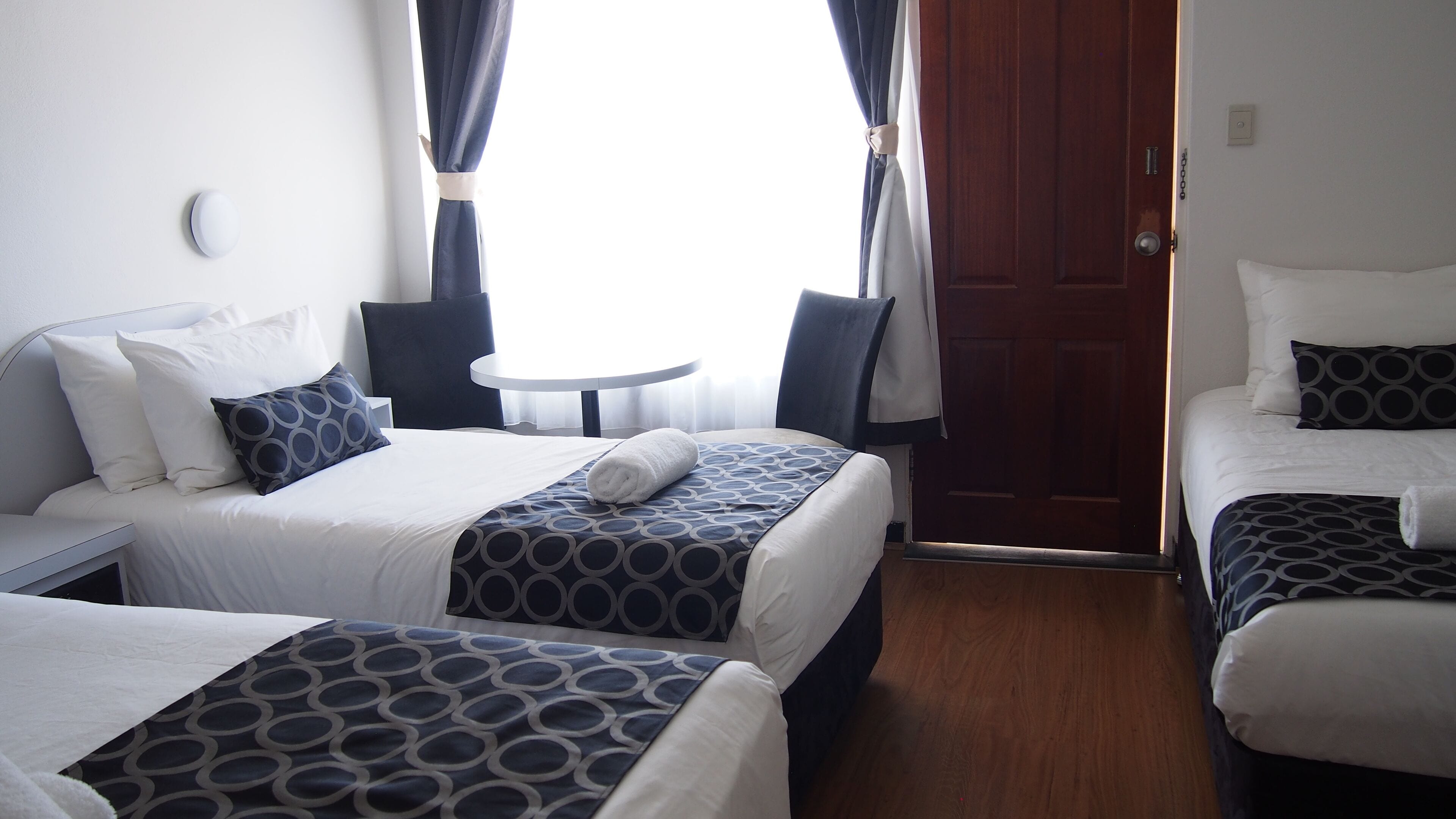 A hotel room with two beds, a small round table, and a door.