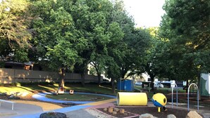 Un parque infantil con macetas hechas de neumáticos, un tobogán azul y amarillo, y una estructura amarilla con forma de pelota.