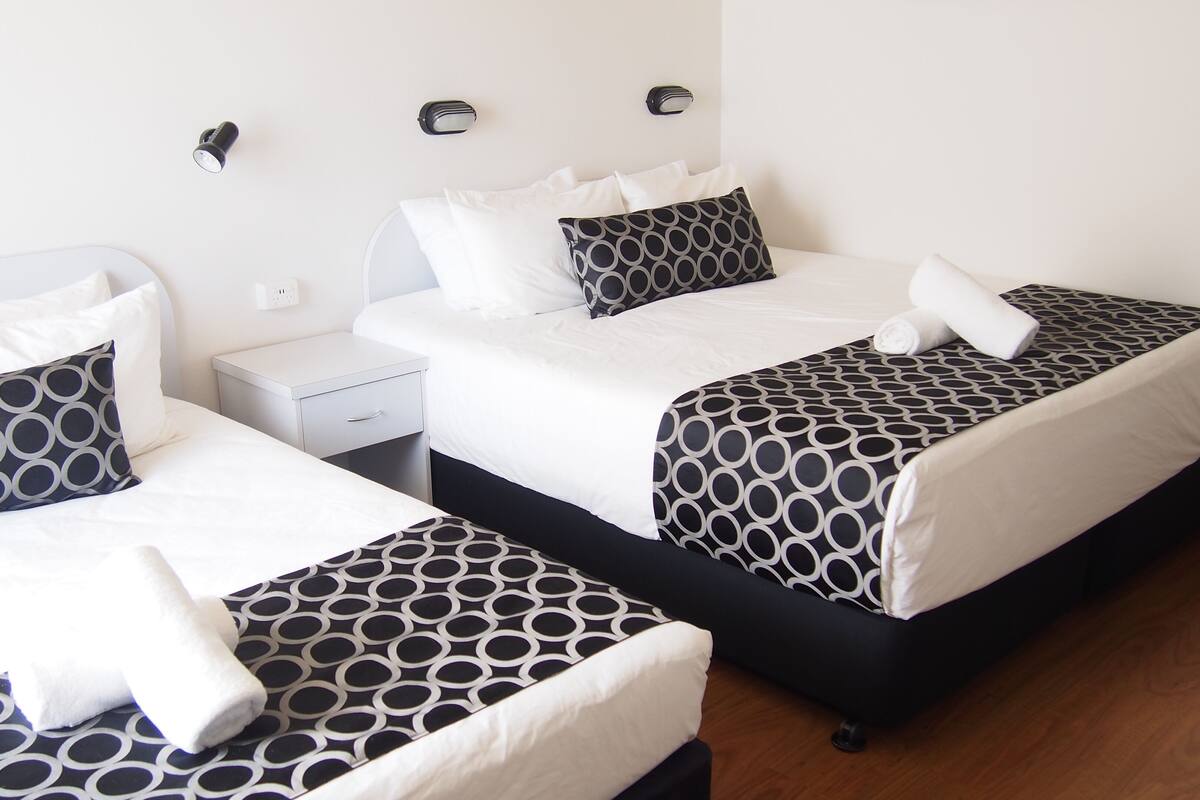 Dos camas con ropa de cama estampada, una mesita de noche y lámparas fijadas en la pared.
