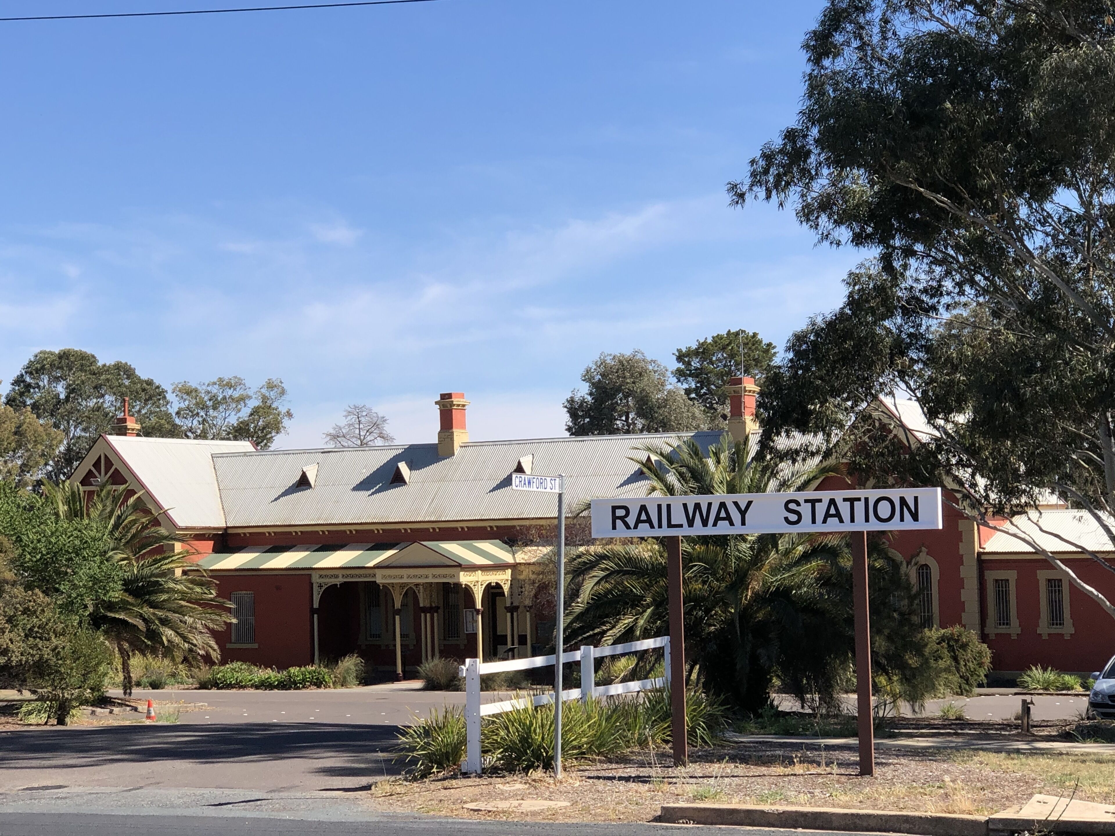 A railway station with a red building, a sign reading "Crawford St", and a white fence.
