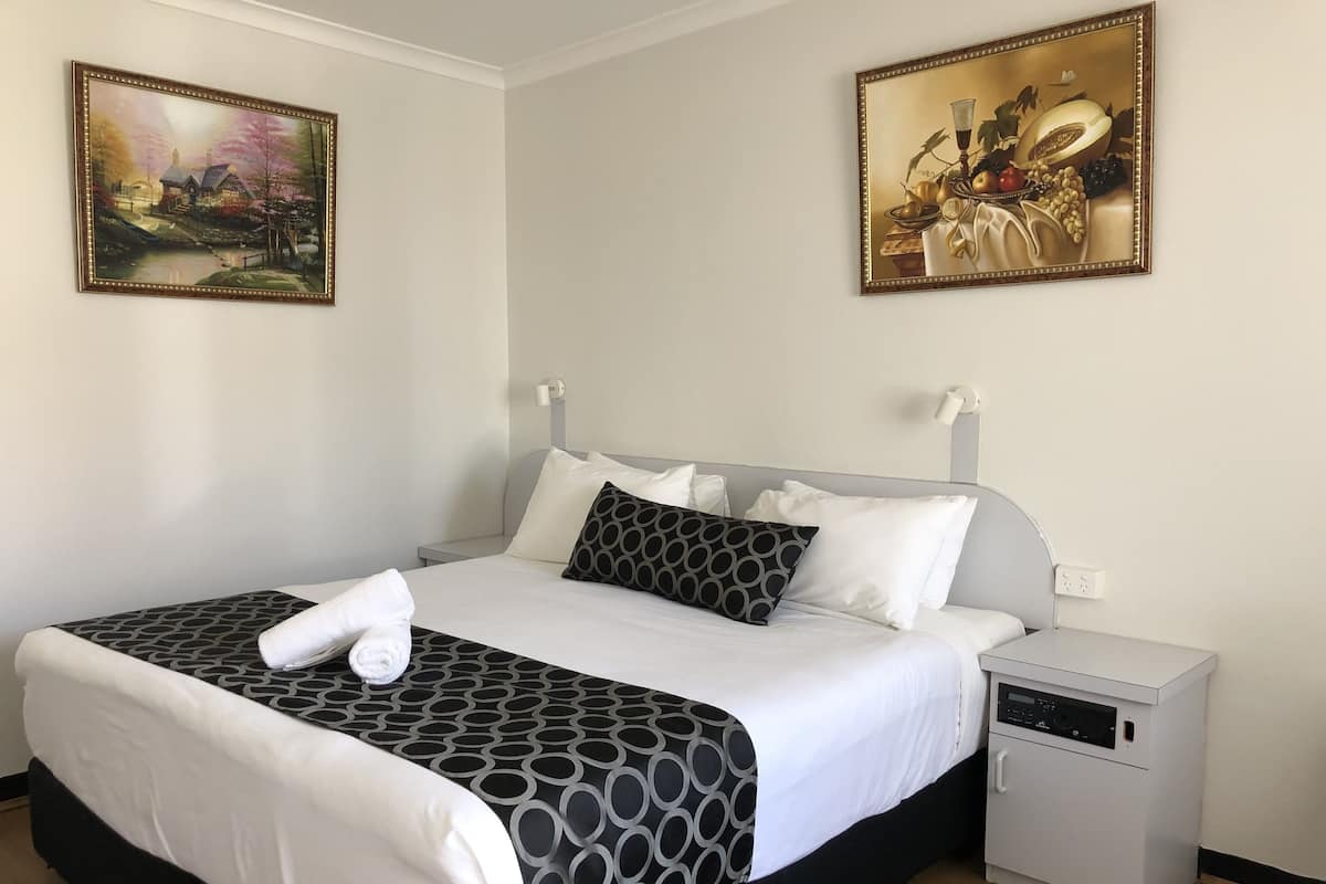 Habitación de hotel con cama, mesita de noche y un armario pequeño blanco.