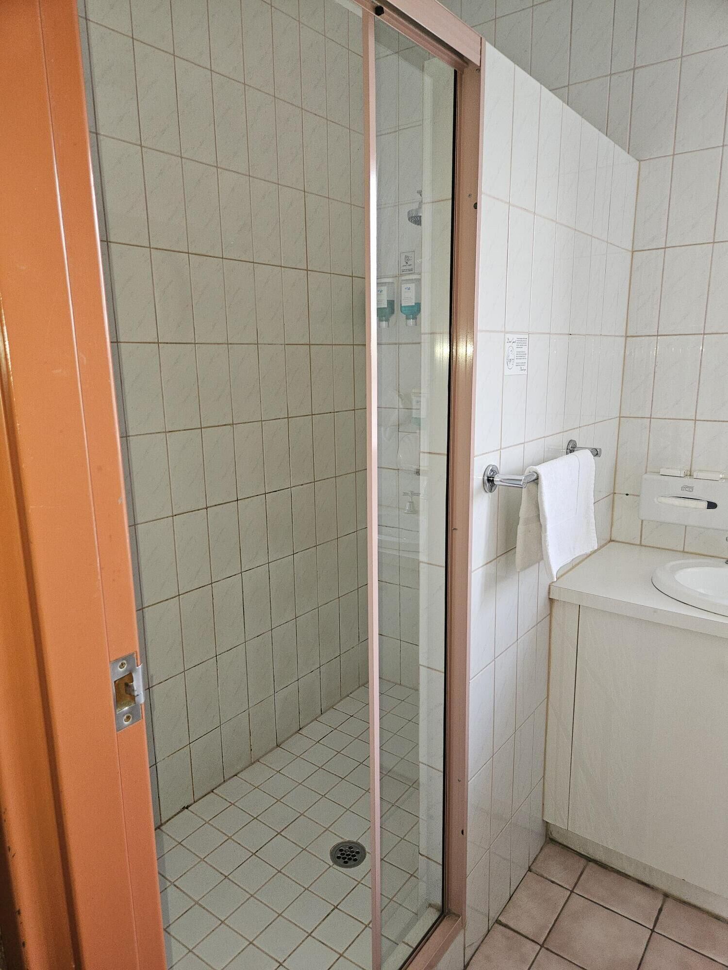 Ein Badezimmer mit Duschkabine aus Glas, einem weißen Waschbecken und einem Handtuch auf einem Halter.