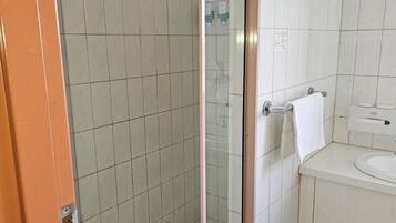 Un baño con cabina de ducha de vidrio, un lavabo blanco y una toalla colgada en un perchero.