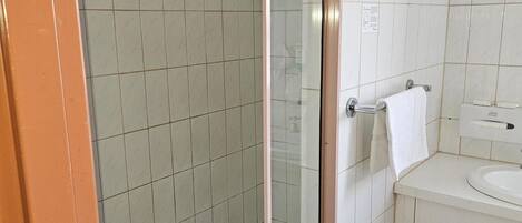 A bathroom with a glass shower enclosure, a white sink, and a towel hanging on a rack.