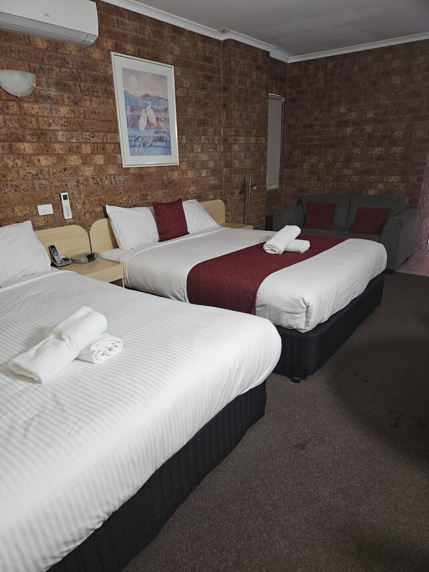 A hotel room with three beds, a brick wall, a painting, and a grey sofa.
