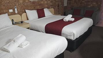 A hotel room with three beds, a brick wall, a painting, and a grey sofa.
