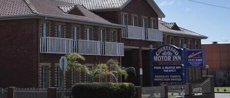 Un edificio de ladrillo con un cartel que indica 'Courtyard Motor Inn', mostrando una piscina y un spa climatizado.